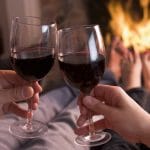 Feet warming at fireplace with hands holding wine